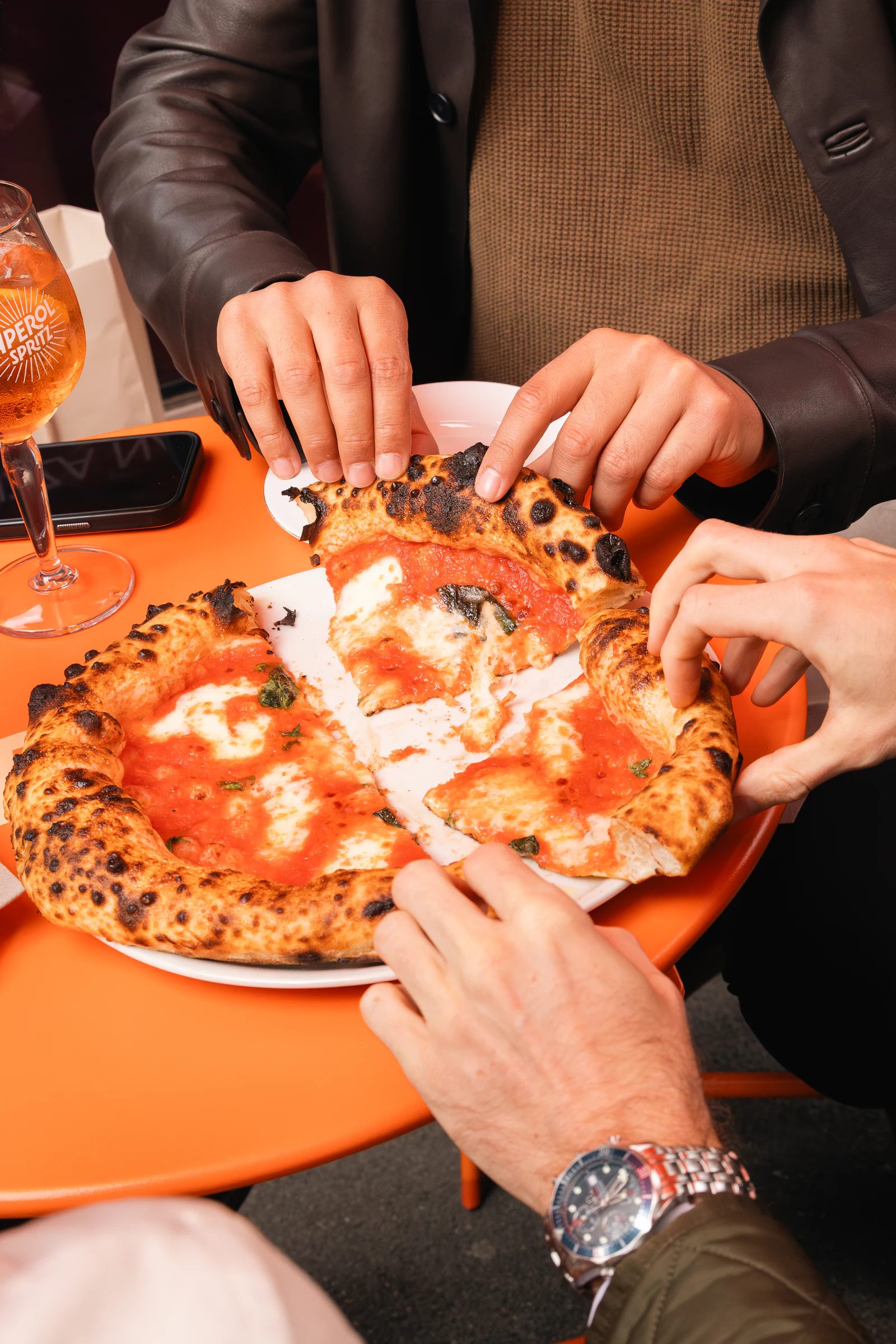 Hände greifen nach Stücken einer Pizza zum Teilen