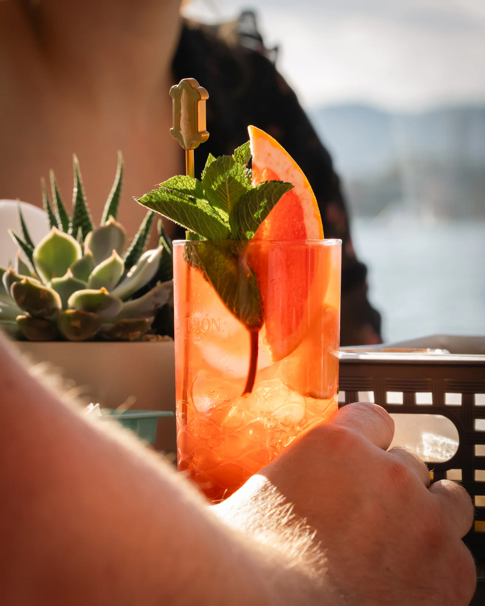 Ein garnierter Cocktail, vor dem Wasser in die Höhe gehalten