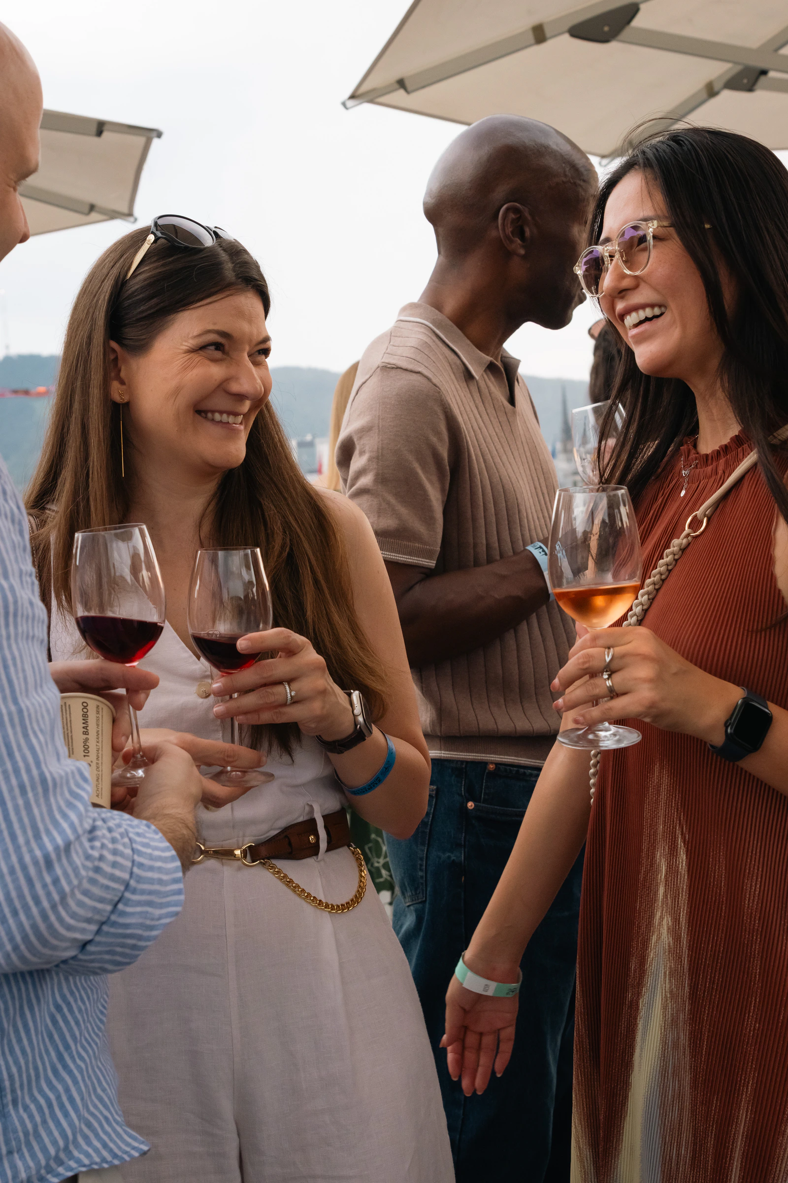 Deux invités discutent autour d’un vin rouge et d’un vin orange, sous les parasols du toit-terrasse